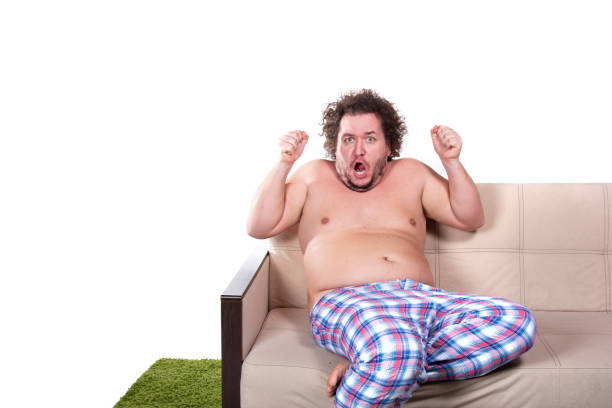 istock Funny fat man watching tv at home. 1564639813