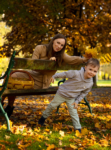Mother and son play in the park in the golden autumn. Young woman sitting on a bench