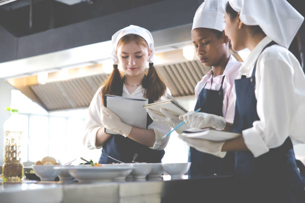 istock take note on book. Cooking class. culinary classroom. group of happy young woman multi-ethnic students are focusing on cooking lessons in a cooking school. 1564672200
