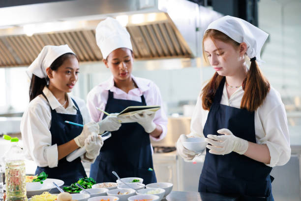 istock take note on book. Cooking class. culinary classroom. group of happy young woman multi-ethnic students are focusing on cooking lessons in a cooking school. 1564672231