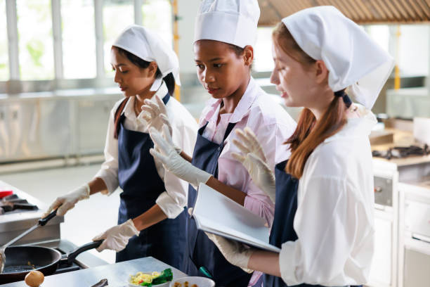 istock take note on book. Cooking class. culinary classroom. group of happy young woman multi-ethnic students are focusing on cooking lessons in a cooking school. 1564672232