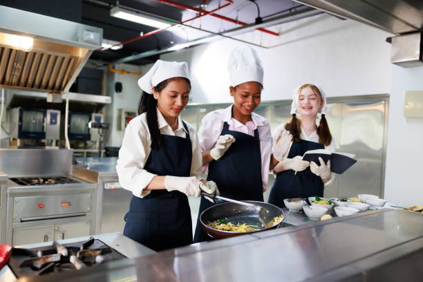 istock take note on book. Cooking class. culinary classroom. group of happy young woman multi-ethnic students are focusing on cooking lessons in a cooking school. 1564672260