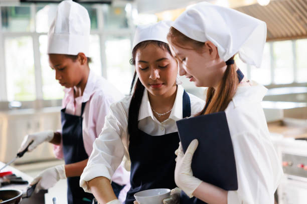 istock take note on book. Cooking class. culinary classroom. group of happy young woman multi-ethnic students are focusing on cooking lessons in a cooking school. 1564672264