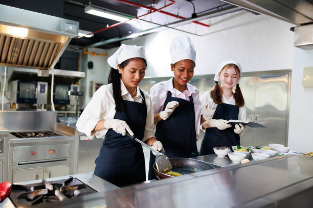 istock take note on book. Cooking class. culinary classroom. group of happy young woman multi-ethnic students are focusing on cooking lessons in a cooking school. 1564672265