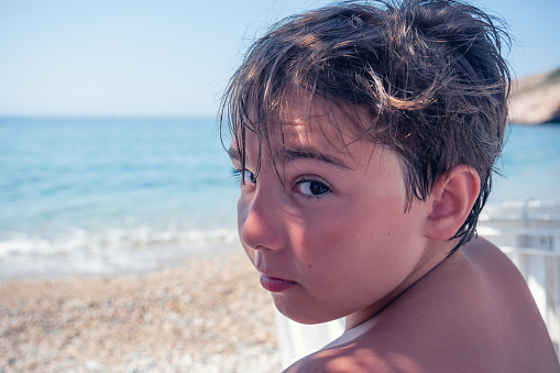 Portrait of boy looking at camera with sunburned skin at the Seashore. Summer vacation, leisure, sea, family vacation, childhood concept.