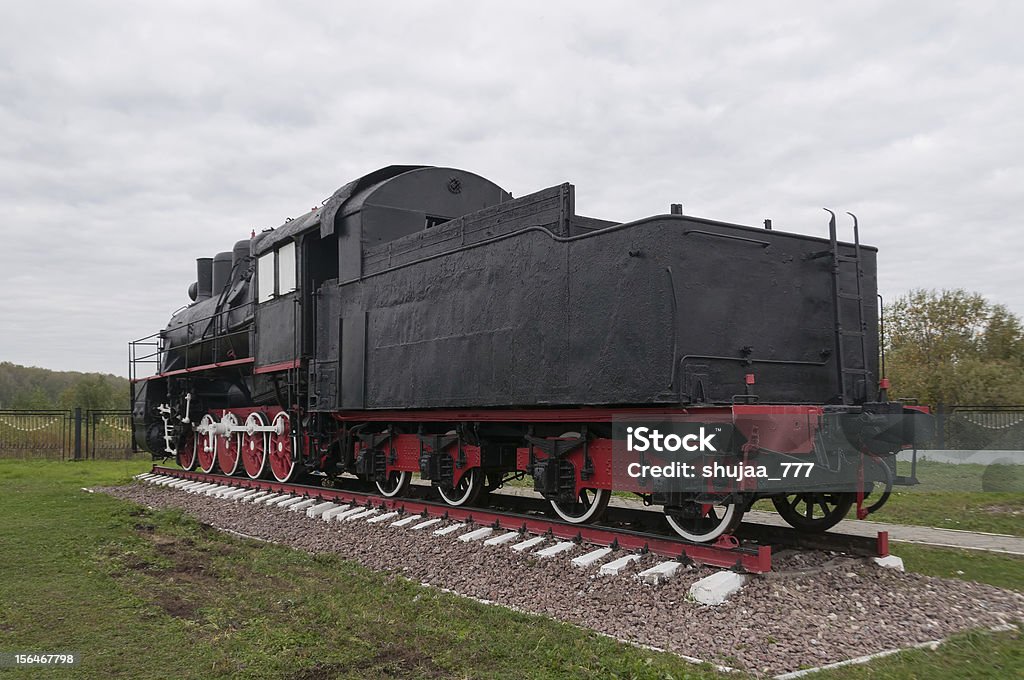 Old black locomotiva a vapor no fundo de céu nublado - Foto de stock de Antigo royalty-free