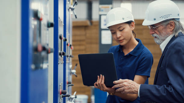 Professional male industrial engineers talk with factory worker while using laptop in manufacturing factory. Working in manufacturing plant or production plant.