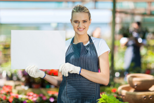 attractive young female florist holding white board in greenhouse