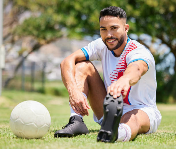 istock Soccer ball, field and man stretching legs on grass for sport training or exercise workout. Portrait of young happy athlete, healthy lifestyle motivation and cardio warm up for football competition 1564721829