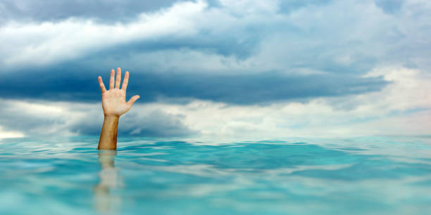 istock SOS, help man drowing, hand on blue rippled ocean, blue cloudy sky background. 1564743421