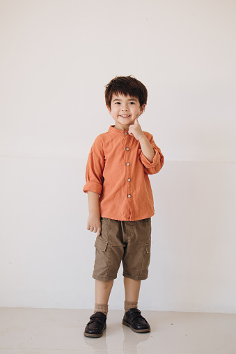 A portrait of a boy wearing an orange polite shirt showing a thoughtful expression.