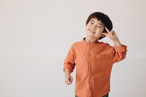A portrait of a boy wearing an orange formal shirt showing a two-finger gesture and looking at the camera.
