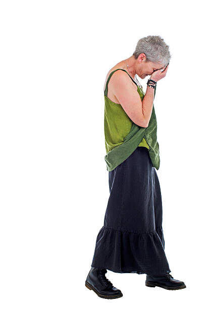 Sad older woman stands in loose flowing long dress Cheerful friendly older woman stands in loose flowing long green linen two piece dress with ruffle. She has short gray hair. Isolated on white background, vertical. embarrassment skirt photos stock pictures, royalty-free photos & images
