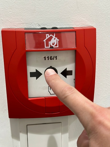 Finger pressing fire alarm emergency button to set of fire alarm