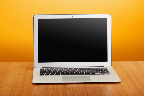 Real laptop computer on wood table and orange background with clipping path for the screen