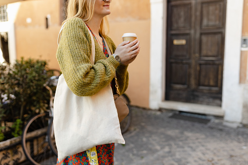 Young Girl holding coffee and white cotton tote bag on old town background. Mockup and zero waste concept. Eco Nature Friendly Style. Environmental Conservation Recycling mock up