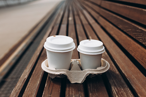 Takeaway paper coffee cups with lids in cardboard holder on wooden bench outdoors