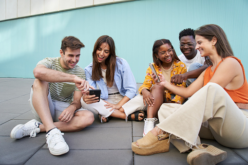 Group of students using mobiles app outdoors and smiling sitting in a floor checking cell phone multimedia or social media.