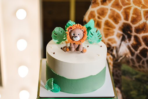 Birthday cake for child. Cake with figure lion decorated green palm leaves for boy or girl. Delicious reception at a birthday party. Concept of festive desserts. Closeup. Decor in style tropical zoo.