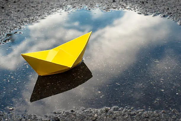 a yellow paper boat in a puddle, representing a dream that begins with simple things