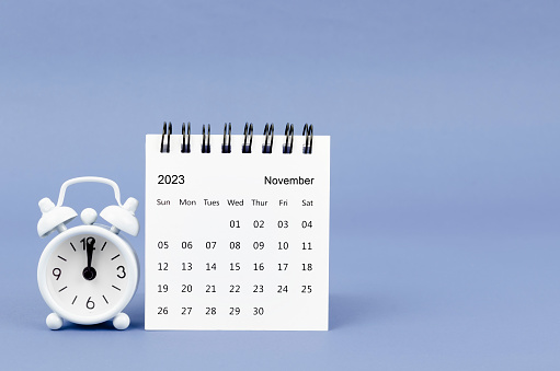 November 2023 desk calendar and alarm clock on blue color background.