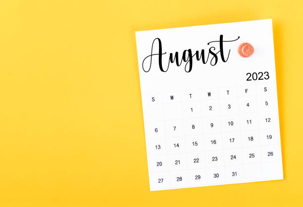 The August 2023 and wooden push pin on yellow background. stock photo