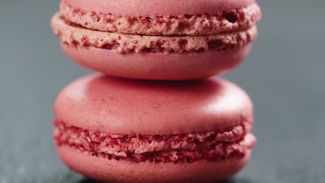 Closeup pan of raspberry red macarons stacked on slate board