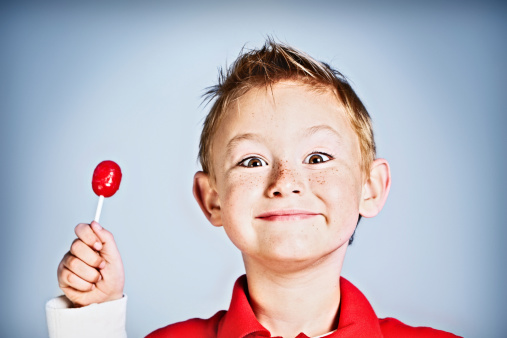 This handsome little boy smiles delightedly as he holds up his delicious red lollipop. 