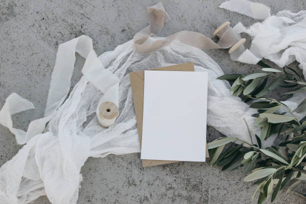 istock Summer wedding stationery mock-up scene. Blank greeting card, invitation template. White silk ribbon, veil. Olive branches and fruit. Grunge concrete background. Mediterranean flat lay, top view. 1564952432