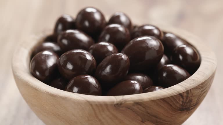 Closeup pan of chocolate covered almonds in wood bowl on table