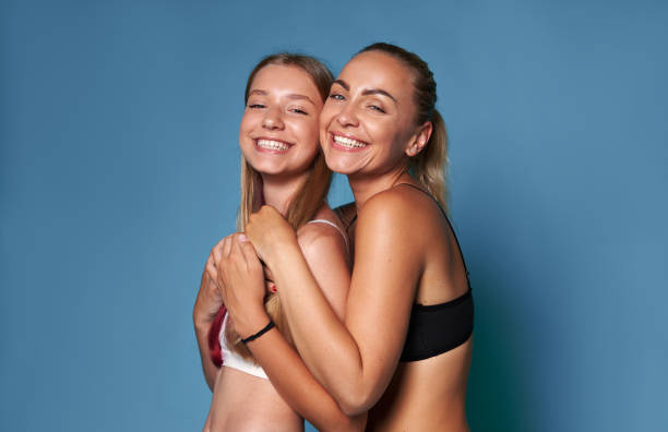 two pretty women, mom and daughter smiling with a beautiful toothy smile, hugging each other, isolated studio background - offspring child toothy smile beautiful imagens e fotografias de stock
