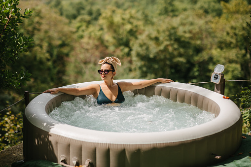 A young woman with a head tie enjoying a view of a Tuscany in September from a hot tub. Visiting Tuscany in September
