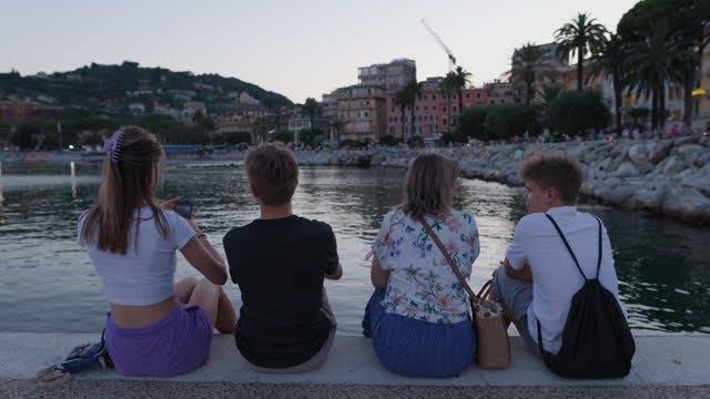 Tourist family sitting on pier in Rapallo, Liguria, Italy.