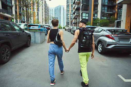 Back view of fashionable man and woman holding hands of each other while walking down street