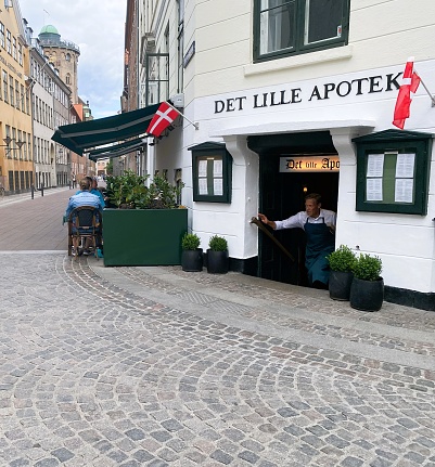 Waiter comes up the stairs from the restaurant to serve the customers sitting outdoors. The photo was taken in Store Kannike Stræde down town Copenhagen, Denmark on July  17th, 2023.