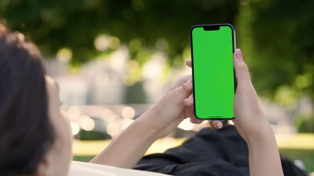 Young Girl Using Phone With Green Mock-up Screen Outside in City Park