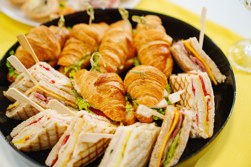 A plate of sandwiches and croissants stuffed with cheese, ham and vegetables. A delicious and simple snack.