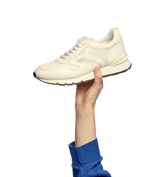 istock A woman's hand holding an ivory sneaker isolated on a white background. Sport and active lifestyle. 1565081110