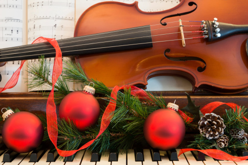 A violin and sheet music sits on a piano that has been decorated for the Christmas holiday.