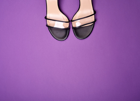 A shot capturing the toes of the summer shoes with clear vamps with black trimming and black-beige insoles. Purple background with copy space.  Fashion blog or magazine concept.