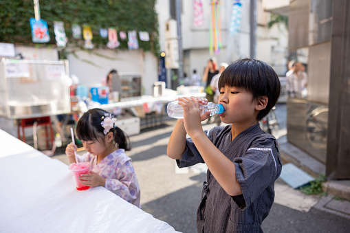 Little sister and brother in Yukata / Jinbei enjoying traditional Japanese summer festival, drinking soda and Kakigori