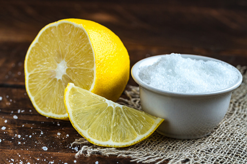 Lemon acid in a white, small plate, a slice of lemon and a juicy lemon on a wooden background. Citric acid