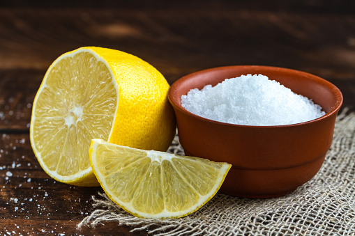 Lemon acid in a brown, small plate, a slice of lemon and a juicy lemon on a wooden background. Citric acid