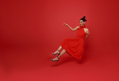 Happy smiling asian woman relaxing floating in mid-air and open hand isolated on red copy space background.