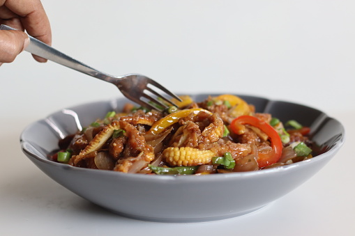 Baby corn chilly. An Indo Chinese dish with crisp fried baby corn in a spicy sauce with sauteed onions and bell peppers. Shot on white background