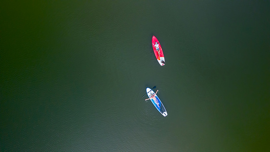 Aerial view of Asian athletic woman on paddle board with friend at lake. Outdoor water sport and travel on summer holiday Thailand.
