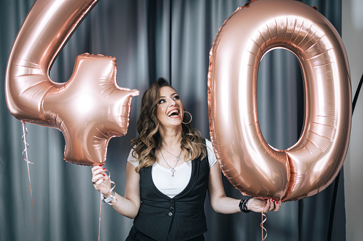 One woman, happy mature woman holding balloons with number 40, it's her 40th birthday.