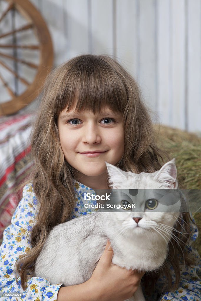 Portrait sincere girl villager with cat on hands in barn Portrait of little sincere friendly blond girl villager sitting with white cat in hands in wooden barn Affectionate Stock Photo