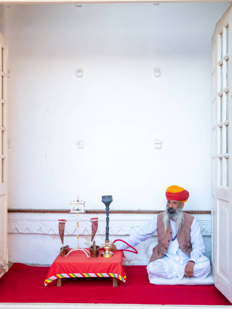 Udaipur, India - December 29, 2022 : Unidentified old aged Rajasthani man in traditional attire smoking using old fashioned method