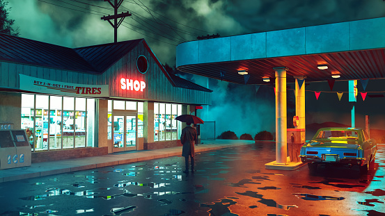 Moody cinematic scene with a man holding an umbrella and wearing trench coat, while he stands next to a retro gas station at night. There are puddles of rain water on the ground. The gas station is open and a sign is lit with the words 